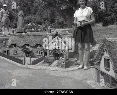 Anni '1950, storico, estivo e una donna che si trova in piedi per una foto accanto a un edificio con tetto in paglia in un villaggio modello, Inghilterra, Regno Unito, un'attrazione turistica tradizionale e popolare nella vita britannica in quest'epoca. Foto Stock