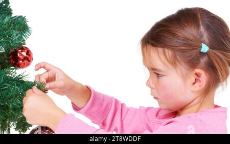 Natale, albero e decorazione con una bambina in studio isolato su uno sfondo bianco per festività. Bambini, vacanza e adorabile Foto Stock