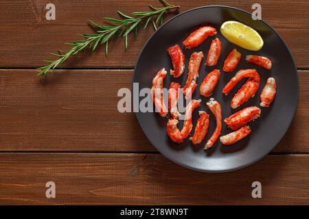 Carne di granchio a fette di rosmarino e limone su piatto grigio su tavola marrone di legno sfondo del piano portapaziente, vista dall'alto, spazio per copiare il testo Foto Stock