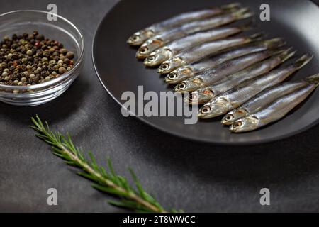 Acciughe europee, hamsa Fresh, diverse piccole miscele di pesce, rosmarino e pepe su piatto grigio su tavola marrone di legno, fondo del piano portapaziente, vista dall'alto, spazio per Foto Stock