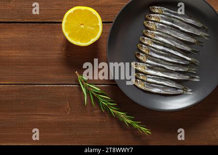 Anchovy european, hamsa Fresh, diversi piccoli pesci su piastra grigia, su tavola marrone di legno sfondo del piano portapaziente, vista dall'alto, spazio per copiare il testo. Foto Stock