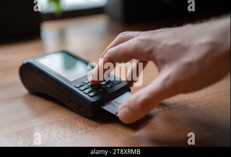 Man palm Typing POS terminal buttons credito pin-code effettuando pagamenti bancari wireless con processo Acquisisci al ristorante Table Cafe al coperto. Concentrati sul machin Foto Stock