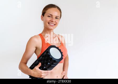 Ritratto di una donna sportiva con un rullo in schiuma in mano davanti a uno sfondo bianco. Foto Stock