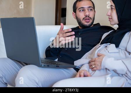 uomini e donne incinte che parlano della gravidanza e di come crescere il bambino mentre usa il notebook in casa indossando il nero e il grigio Foto Stock