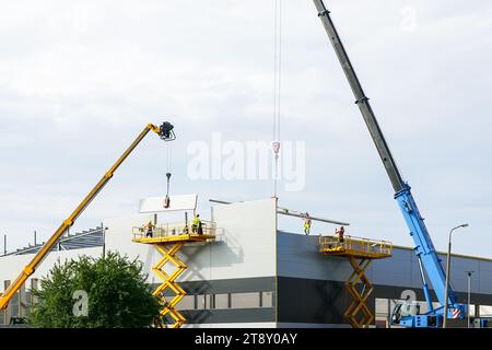 Montaggio di pareti a pannelli sandwich e tetto mediante due gru telescopiche a braccio e due sollevatori a forbice semoventi Foto Stock