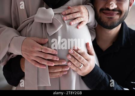 L'uomo arabo sta ascoltando il pancino della sua bella moglie incinta e sorridendo Foto Stock