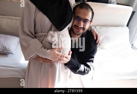 L'uomo arabo sta ascoltando il pancino della sua bella moglie incinta e sorridendo Foto Stock