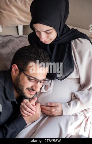 L'uomo arabo sta ascoltando il pancino della sua bella moglie incinta e sorridendo Foto Stock