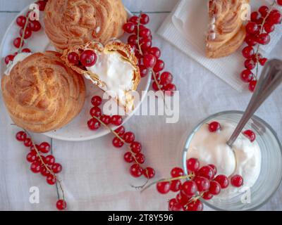 Dolce e delizioso tavolo da dessert con dolce choux rotondo (eclairs) riempito con crema crema pasticcera bianca e decorato con ciuffi di ribes rosso Foto Stock