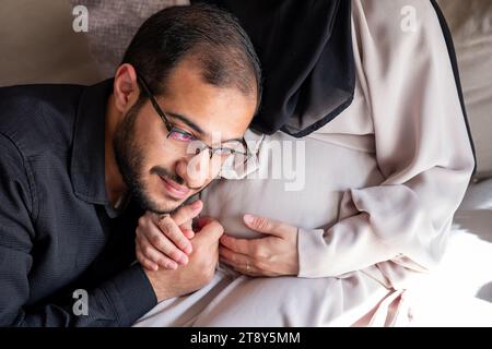 L'uomo arabo sta ascoltando il pancino della sua bella moglie incinta e sorridendo Foto Stock