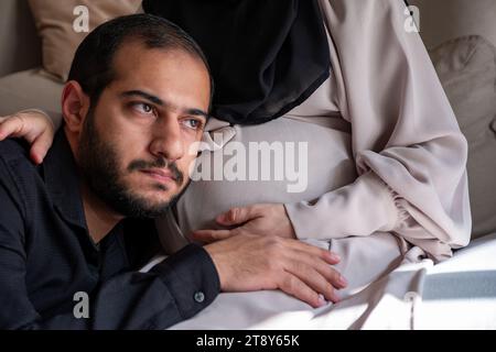 L'uomo arabo sta ascoltando il pancino della sua bella moglie incinta e sorridendo Foto Stock