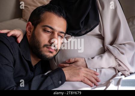 L'uomo arabo sta ascoltando il pancino della sua bella moglie incinta e sorridendo Foto Stock