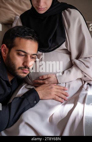 L'uomo arabo sta ascoltando il pancino della sua bella moglie incinta e sorridendo Foto Stock