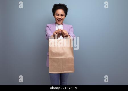 giovane donna latina di successo con i capelli afro vestita con una giacca che regge un pacco artigianale dalla consegna del cibo Foto Stock