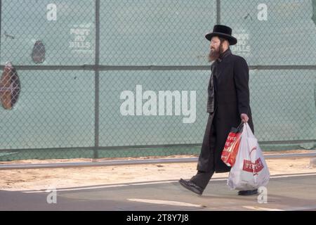 Un ebreo ortodosso, probabilmente del gruppo Satmar, porta borse della spesa e cammina davanti a un cantiere a Brooklyn, New York. Foto Stock
