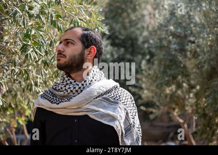 ritratto per uomo che indossa keffiyeh in un campo di ulivi con sfondo nero e camicie nere anche con espressione facciale arrabbiata Foto Stock