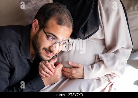 L'uomo arabo sta ascoltando il pancino della sua bella moglie incinta e sorridendo Foto Stock