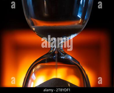 Primo piano di una clessidra su uno sfondo caldo e luminoso con sabbia che scende Foto Stock