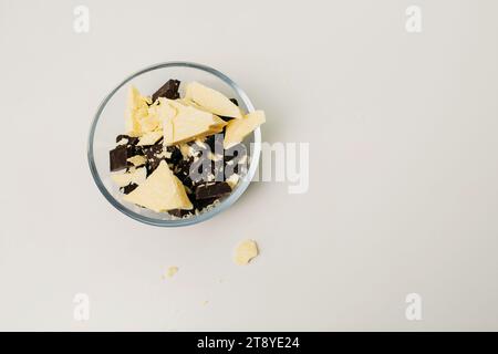 Pezzi di cioccolato e burro di cacao in un piatto di vetro su sfondo bianco. Primo piano. Vista dall'alto. Foto Stock