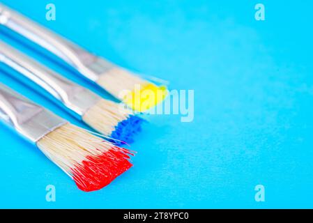 Pennelli con vernice rossa, blu e gialla su sfondo blu Foto Stock