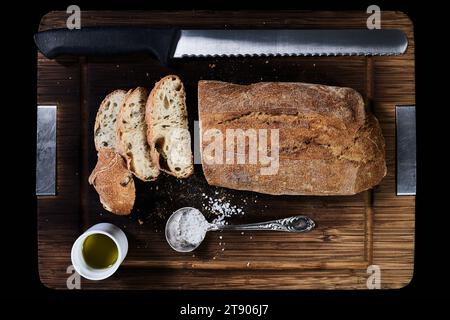 Composizione con pane, coltello, olio d'oliva e sale grosso su tagliere di legno, vista dall'alto Foto Stock