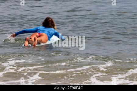 Vista posteriore di una donna che rema su un'onda sdraiata sopra una tavola da surf. Foto Stock