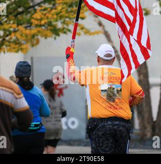 Babylon, New York, USA - 22 ottobre 2023: Un uomo che tiene in mano una bandiera americana per strada mentre corre una maratona. Foto Stock