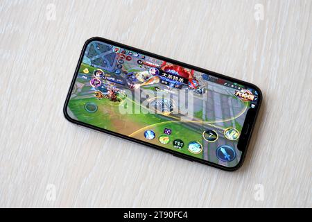 Honor of Kings gioco iOS per dispositivi mobili su schermo dello smartphone iPhone 15 su un tavolo di legno durante il gioco mobile. Giochi e intrattenimento mobili su dispositivi portatili Foto Stock