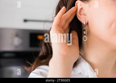 Gioielli e orecchini ravvicinati in un bellissimo orecchio femminile - accessori da donna, orecchini alla moda in argento. Gioielli fatti a mano Foto Stock