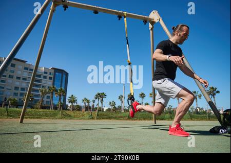 Uomo muscoloso durante l'allenamento fisico allenare il peso corporeo con cinghie di sospensione TRX. Atletico che fa affondi, pompando i muscoli delle gambe. Gente, acti Foto Stock