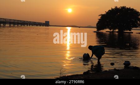 Silhouette donna che lava piatti nel fiume nel pomeriggio durante il tramonto a Mukutmanipur, India Foto Stock