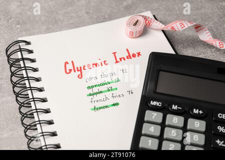 Indice glicemico. Notebook con informazioni, metro a nastro e calcolatrice su tavolo grigio chiaro, primo piano Foto Stock