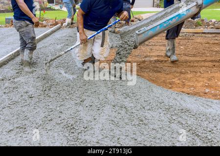 Con l'ausilio di personale addetto alla miscelazione del calcestruzzo, il cemento bagnato è stato versato sul vialetto di accesso della nuova casa Foto Stock