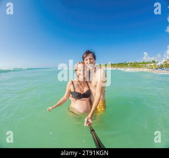 In mezzo al tranquillo mare turchese, una donna incinta e suo marito condividono un momento sereno, celebrando la bellezza dell'imminente genitorialità nel Foto Stock