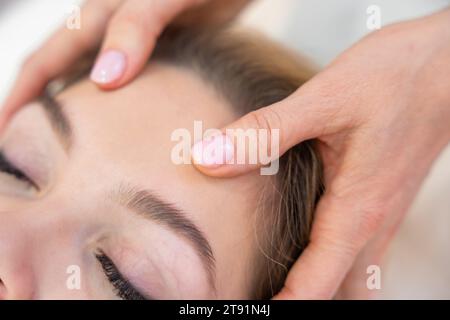 Vista ravvicinata delle mani dei guaritori che eseguono la terapia con barre di accesso leggermente toccate sulla testa di una giovane donna, stimolando pensieri ed emozioni di cambiamento positivo Foto Stock