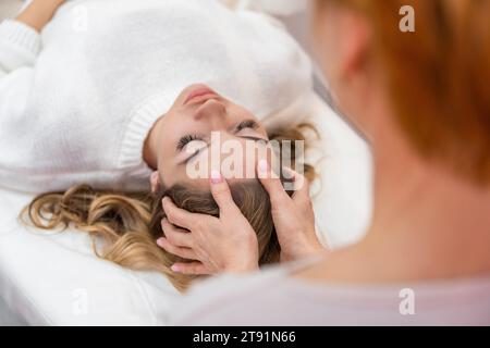 La guaritrice esegue la terapia con barre di accesso leggermente toccate sulla testa di una giovane donna, stimolando i pensieri positivi e le emozioni nel salone. Alternativa Foto Stock