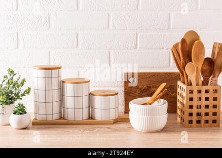 Splendido sfondo da cucina con set di taglieri, cucchiai in legno, ciotole, eleganti vasetti in ceramica. Vista frontale. Cucina ecocompatibile. Foto Stock