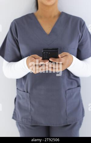 Metà sezione del medico femminile birazziale che indossa scrub usando smartphon in ospedale Foto Stock