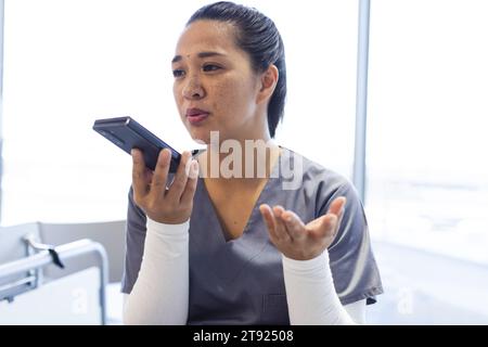 Medico donna birazziale che parla su smartphone a letto in ospedale Foto Stock