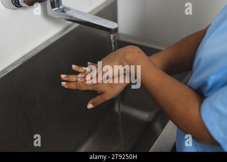 Sezione intermedia di medico birazziale che indossa scrub lavarsi le mani in sala operatoria Foto Stock