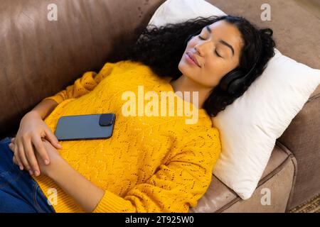 Donna birazziale con cuffie e smartphone sdraiati sul divano a casa Foto Stock