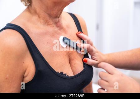 Medico donna che mette donna irriconoscibile con problemi cardiaci sottoposti a test ECG Holter monitor con dispositivo innovativo sul torace Foto Stock