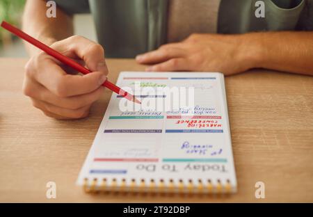 Foto ravvicinata di un uomo d'affari che scrive una lista di cose da fare nel suo blocco note seduto al tavolo. Foto Stock