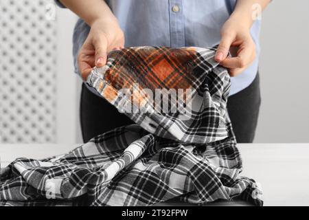 Donna che mostra macchie di salsa sulla camicia al tavolo bianco su sfondo sfocato, primo piano Foto Stock