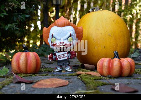 Funko Pop action figure di Pennywise clown malvagio con lo skateboard sanguinoso tratto dal film horror IT. Halloween, stagione spettrale, zucche, muschio, foglie autunnali. Foto Stock