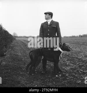 Hare Coursing. The Slipper, Wayne Drew con due levrieri che indossano collari rossi e bianchi. Guarda la siepe verso un gruppo di battitori che guidano lepri, una alla volta, verso il campo di pratica. Il Cotswold Coursing Club Meet, vicino a Kilkenny, Gloucestershire 2000s 2002 HOMER SYKES Foto Stock