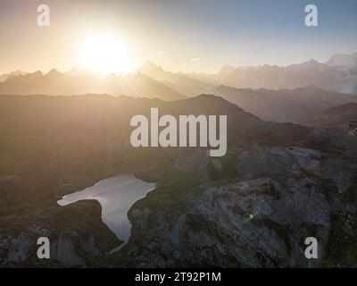 Al tramonto un drone cattura la bellezza serena del lago Anterne. La luce dorata si riflette sulle acque tranquille circondate da lussureggiante vegetazione e alte alpi. Foto Stock