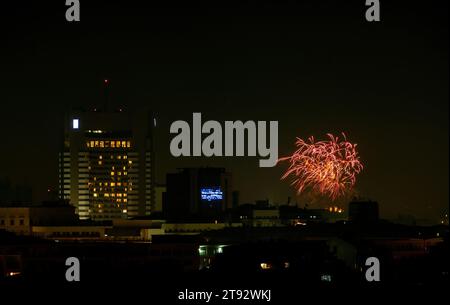 I colorati fuochi d'artificio illuminano il cielo notturno sopra un vivace paesaggio urbano Foto Stock