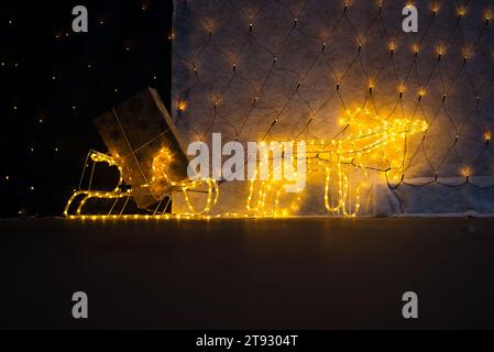 Immergiti nel fascino stravagante di una renna illuminata che tira una slitta adornata da luci scintillanti e un regalo di Natale dorato. Il thir inferiore Foto Stock