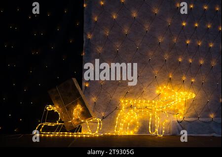 Immergiti nel fascino stravagante di una renna illuminata che tira una slitta adornata da luci scintillanti e un regalo di Natale dorato. Il thir inferiore Foto Stock